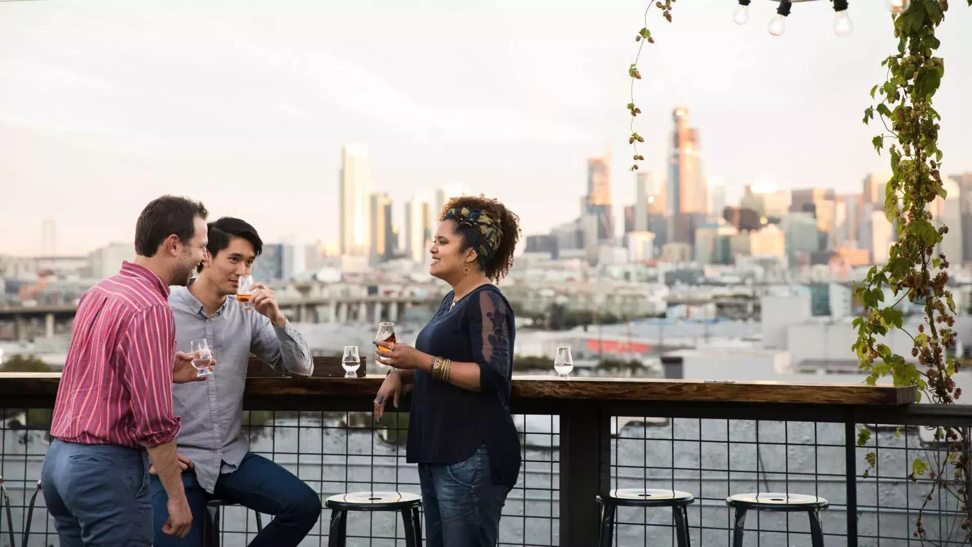 在贝博体彩app锚蒸馏公司的屋顶露台上，三个人围坐在一张户外桌子旁, California.